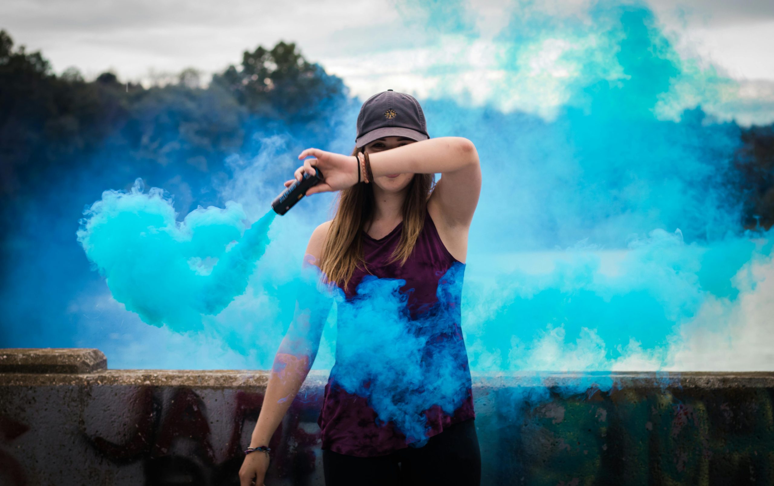 Duda por emociones fuera de control A stylish woman surrounded by bright blue smoke outdoors, creating a dynamic fashion statement.